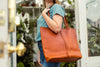 Woman carrying the Cecilia handmade leather Tote in Persimmon on her shoulder with strap closure
