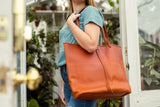 Woman carrying the Cecilia handmade leather Tote in Persimmon on her shoulder with strap closure