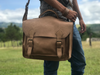 Man carrying Handmade leather luxury work briefcase with two buckle closures and long shoulder strap front view in stone